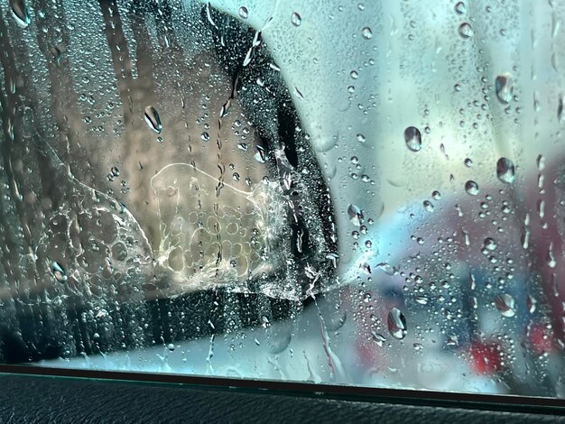 Homem lavando carro no centro de serviços de carro, vidro da janela molhado de gotas de água de lavagem fluindo