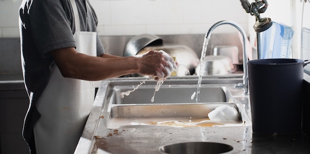 Homem lavando louça na pia do restaurante. as pessoas também estão lavando a louça solução de limpeza