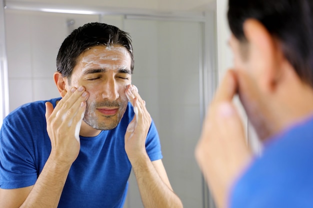 Homem lavando o rosto com sabonete de limpeza facial no banheiro