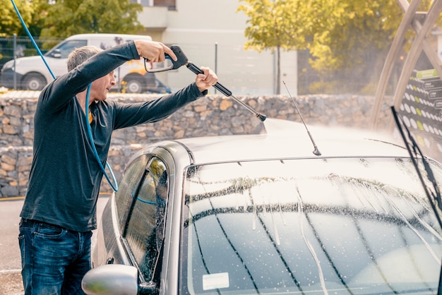 Homem lavando seu carro usando um jato de água de alta pressão