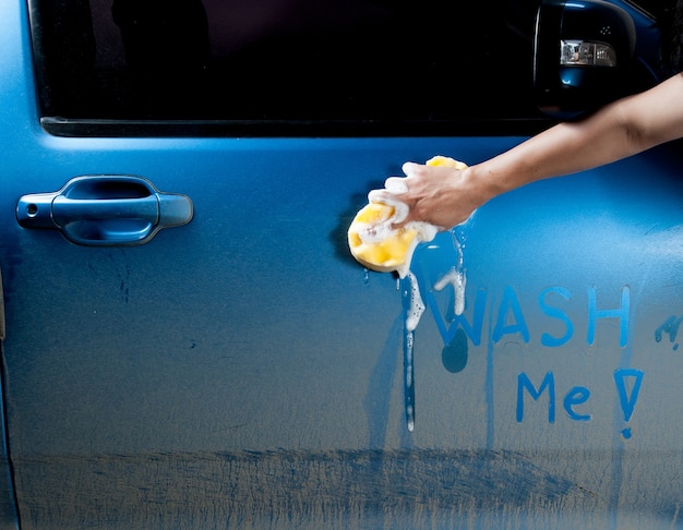 homem lavando um carro azul e sabão com uma esponja.