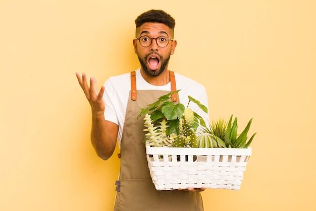 Homem legal afro se sentindo extremamente chocado e surpreso com o conceito de jardineiro e planta