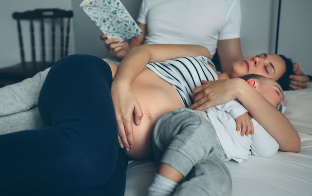 Homem lendo enquanto sua esposa grávida e filho estão dormindo