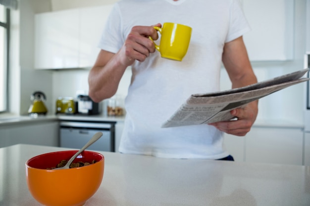 Homem lendo jornal enquanto tomando café na cozinha