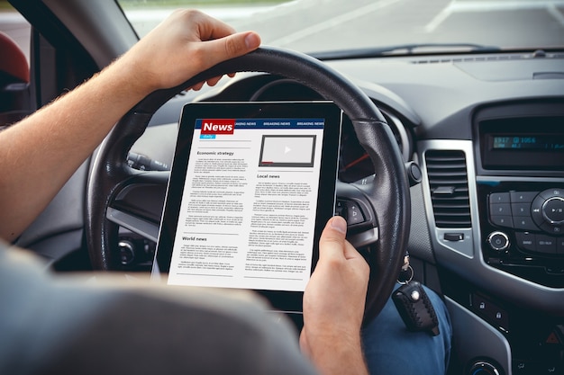 Homem lendo notícias com um tablet na mão ao volante do carro