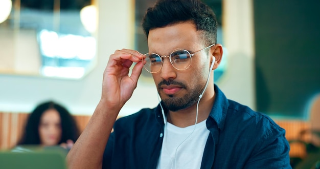 Homem lendo óculos e café para pesquisa on-line trabalho remoto e revisão de site e análise Trabalhador freelancer ou designer em café ou restaurante com computador e música para informações na internet