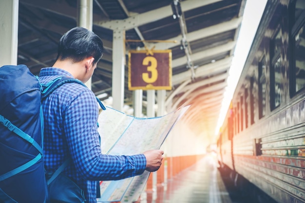Homem lendo um mapa enquanto está de pé na plataforma da estação ferroviária