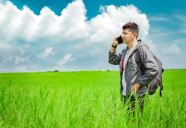 Homem ligando pelo celular, jovem no campo ligando pelo celular, jovem mochileiro com telefone celular no campo e espaço de cópia