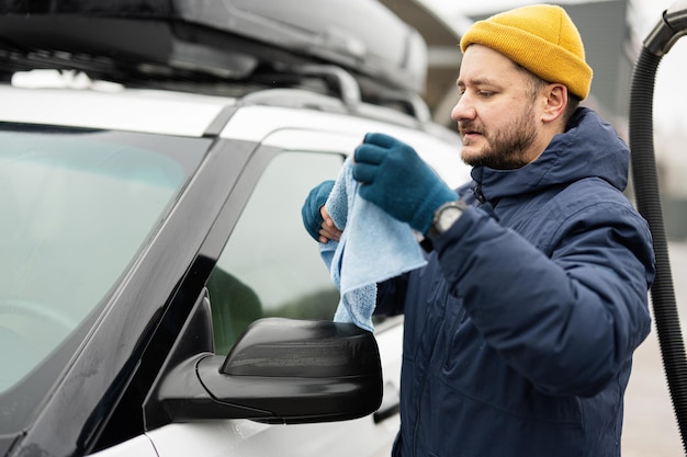 Homem limpa carro SUV americano com um pano de microfibra após lavagem em tempo frio