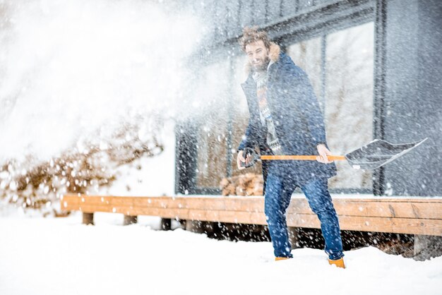 Homem limpando neve perto da casa