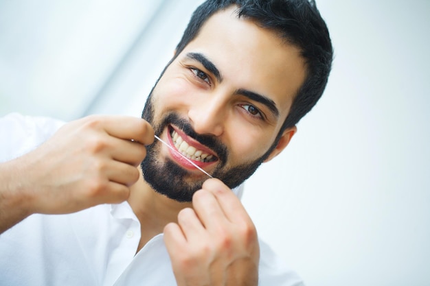 Homem lindo e sorridente usando fio dental saudáveis dentes brancos