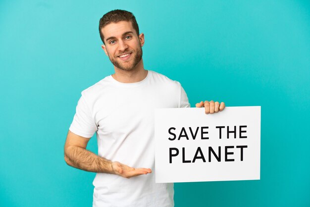 Homem loiro bonito isolado segurando um cartaz com o texto Salve o planeta e apontando-o