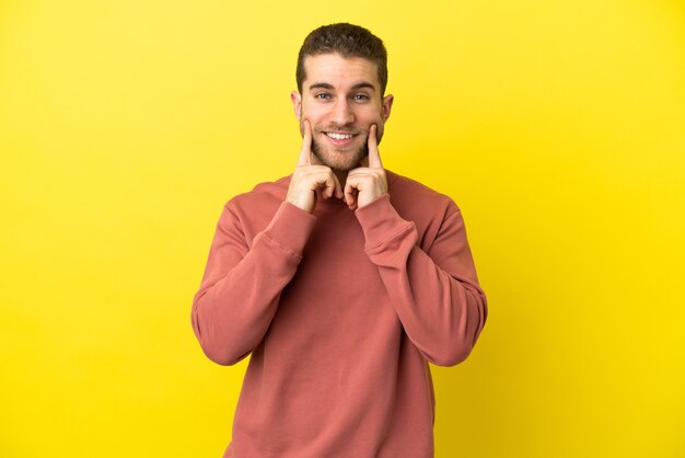 Homem loiro bonito sobre fundo amarelo isolado sorrindo com uma expressão feliz e agradável