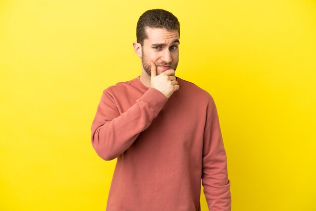 Homem loiro bonito sobre fundo amarelo isolado tendo dúvidas