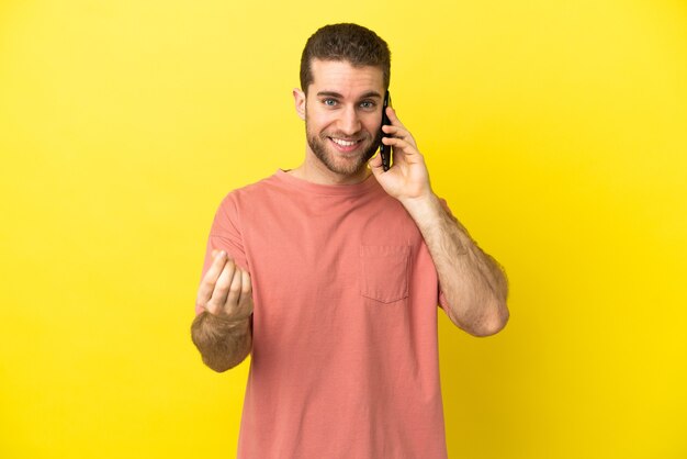 Homem loiro bonito usando telefone celular sobre fundo isolado fazendo gesto de dinheiro