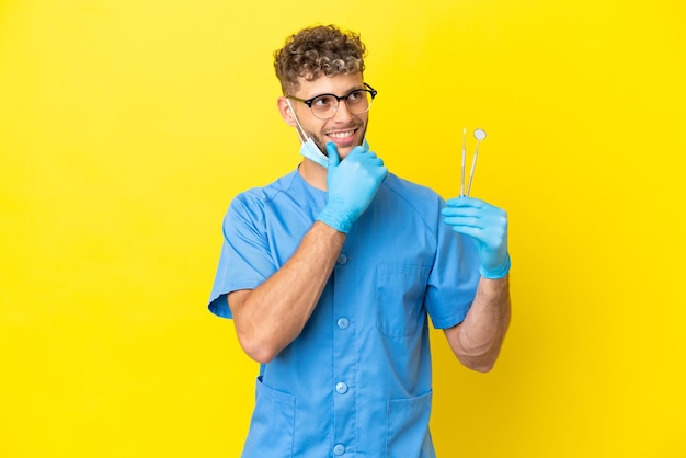 Homem loiro de dentista segurando ferramentas isoladas no fundo e olhando para cima