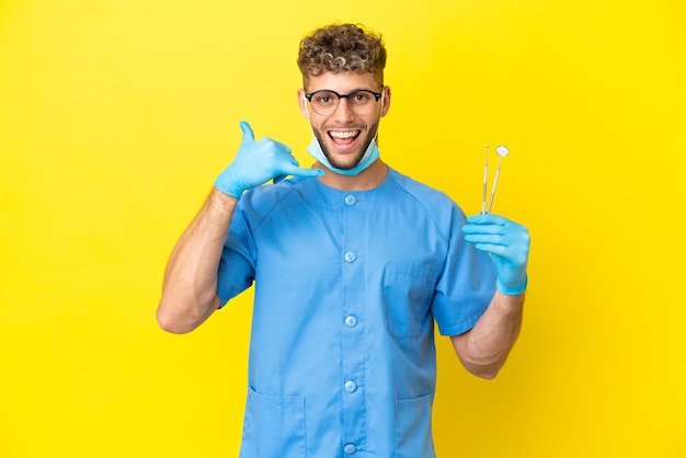 Homem loiro de dentista segurando ferramentas isoladas no fundo, fazendo gestos de telefone. Ligue-me de volta sinal