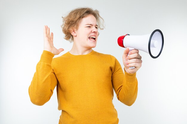 Homem loiro ondulado gritando notícias em um megafone em um fundo branco do estúdio.