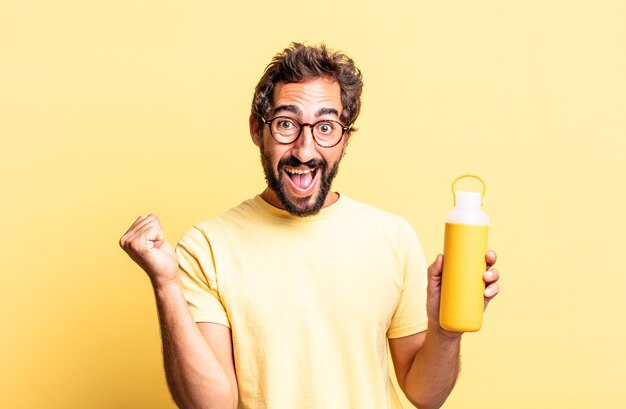 Homem louco expressivo chocado, rindo e comemorando o sucesso com uma garrafa térmica de chá