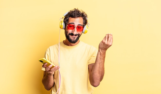 Homem louco expressivo fazendo capice ou gesto de dinheiro, dizendo para você pagar com fones de ouvido