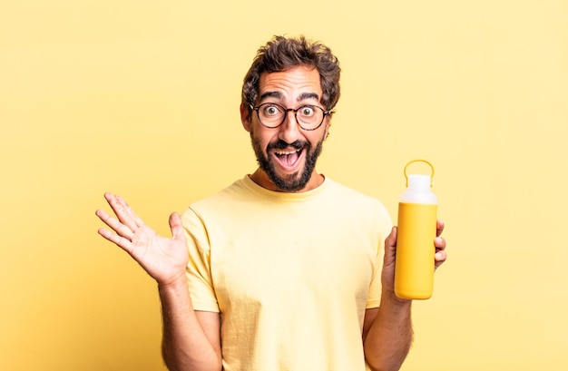 Homem louco expressivo se sentindo feliz e surpreso com algo inacreditável com uma garrafa térmica de chá