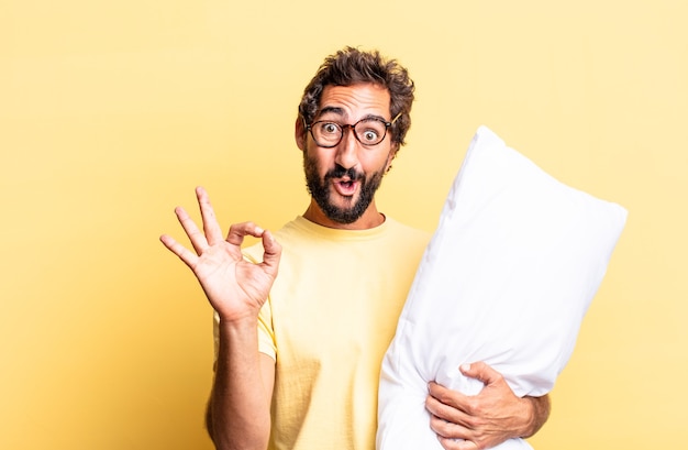 Homem louco expressivo se sentindo feliz, mostrando aprovação com um gesto de ok e segurando um travesseiro