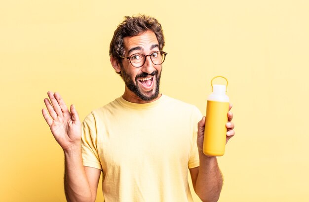 homem louco expressivo sorrindo feliz, acenando com a mão, dando as boas-vindas e cumprimentando você com uma garrafa térmica de chá