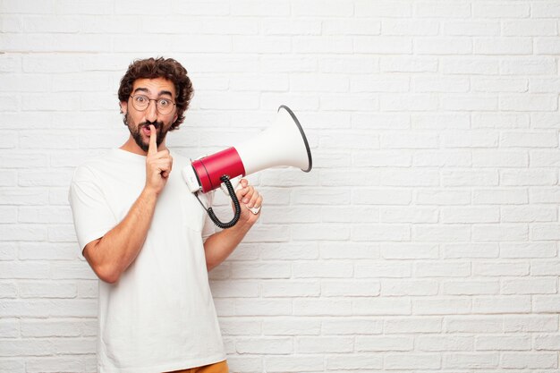 Homem louco novo com um megafone contra a parede de tijolo.