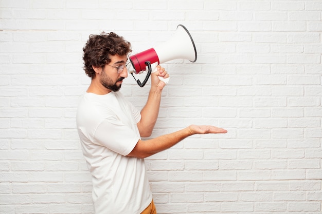 Homem louco novo com um megafone contra a parede de tijolo.