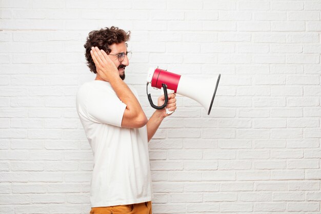 Homem louco novo com um megafone contra a parede de tijolo.