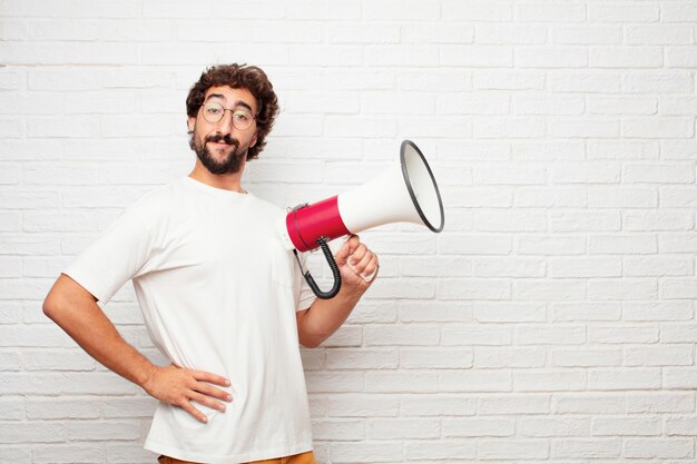 Homem louco novo com um megafone contra a parede de tijolo.