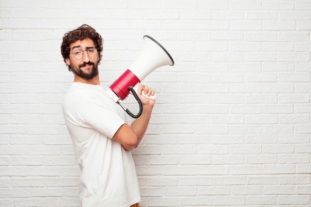 Homem louco novo com um megafone contra a parede de tijolo.