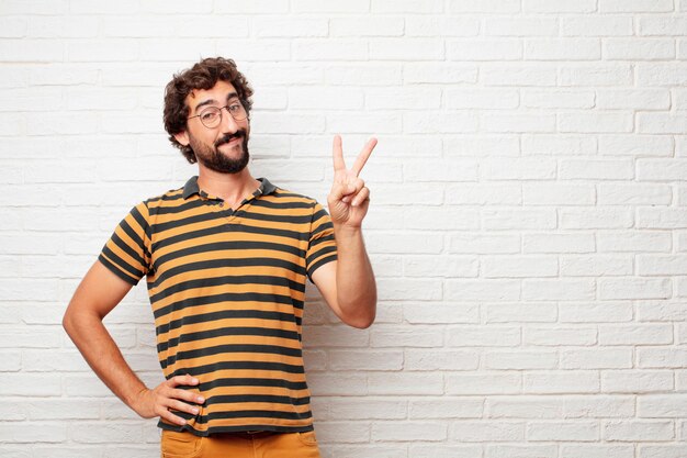 Homem louco ou bobo jovem gesticulando e expressando emoções contra o fundo da parede de tijolo