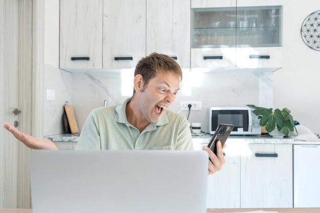 Homem louco zangado gritando gritando e discutindo falando no smartphone enquanto trabalha no laptop online em