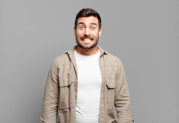 Homem louro adulto bonito parecendo feliz e bobo com um sorriso largo, divertido e maluco e olhos bem abertos