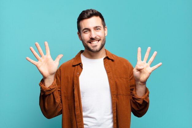 Homem louro adulto bonito sorrindo e parecendo amigável, mostrando o número nove ou nono com a mão para a frente, em contagem regressiva