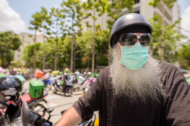 Homem maduro barbudo hipster com óculos de sol e máscara pensando enquanto andava de moto