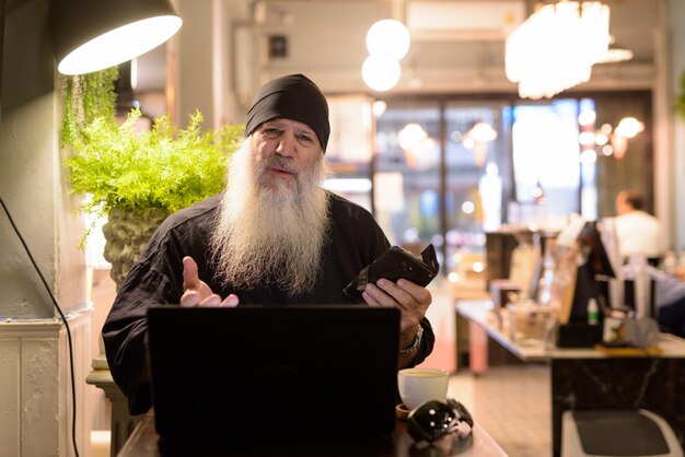 Homem maduro barbudo hipster usando laptop e parecendo confuso na cafeteria