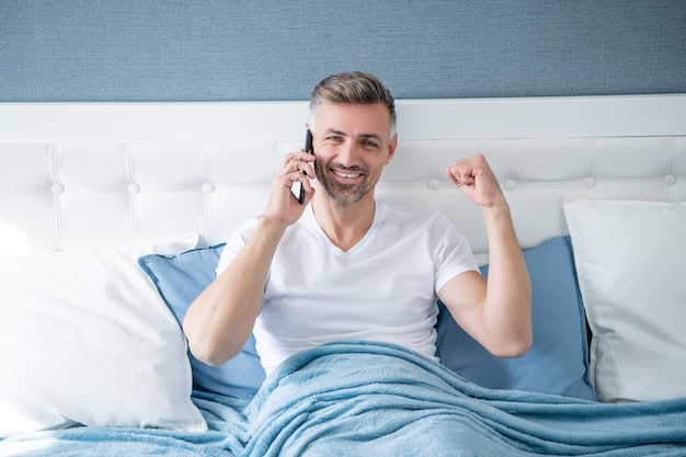 Homem maduro bem sucedido na cama falando no telefone