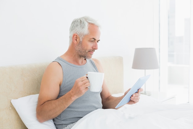 Homem maduro com tableta digital e mesa de café na cama