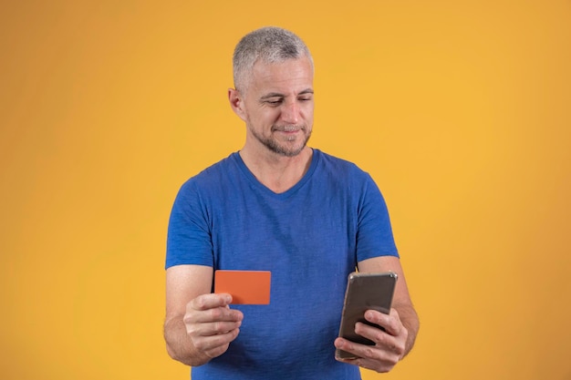 Homem maduro com um cartão de crédito nas mãos fazendo compras pelo celular online