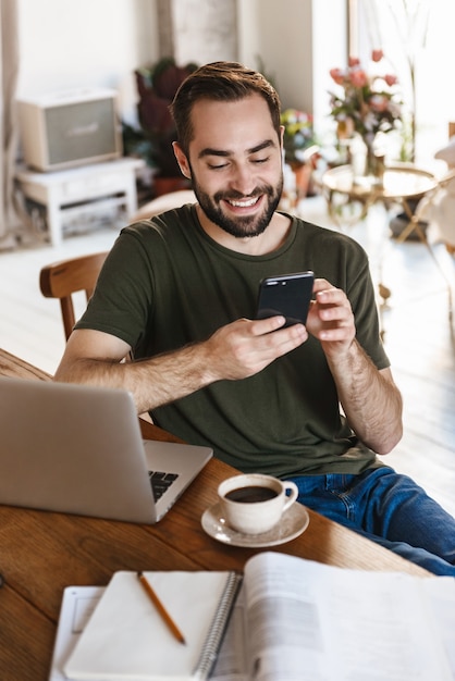 homem maduro de sucesso em roupas casuais usando laptop e smartphone enquanto trabalhava em apartamento