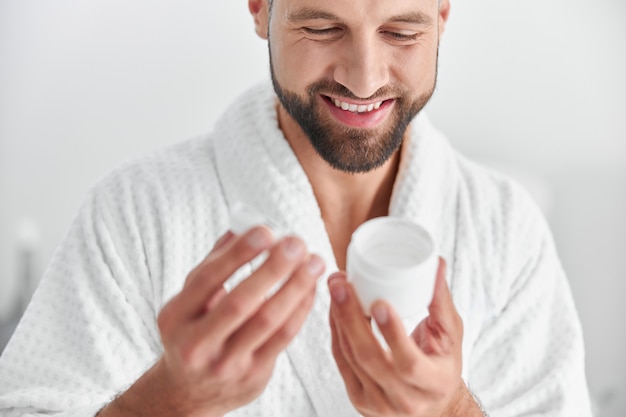 Homem maduro e feliz olhando para um frasco aberto de creme em uma clínica cosmetológica profissional