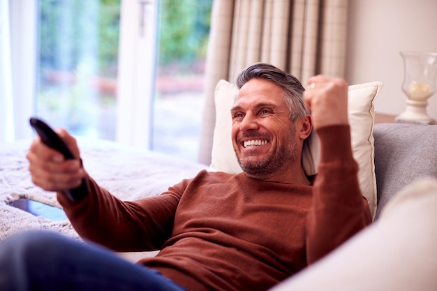 Homem maduro em casa relaxando no sofá assistindo esportes na TV