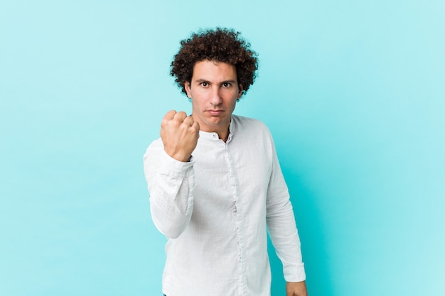 Homem maduro encaracolado novo que veste uma camisa elegante que mostra o punho à câmera, expressão facial agressiva.