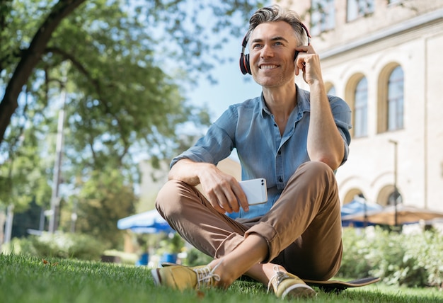 Homem maduro feliz ouvindo música em fones de ouvido, relaxando no parque