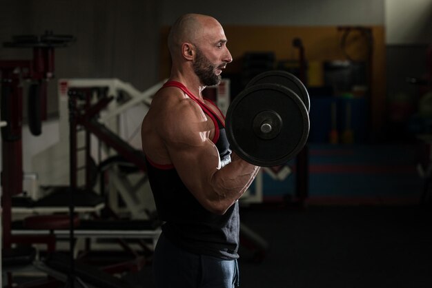 Homens maduros fazendo exercícios de supino inclinado com halteres na  academia