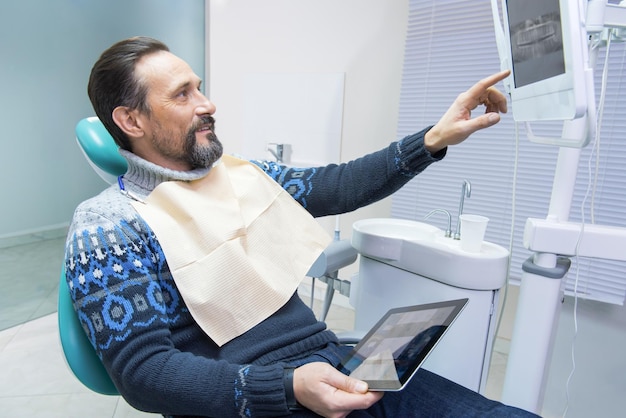 Foto homem maduro no consultório do dentista segurando tecnologias e remédios para tablet