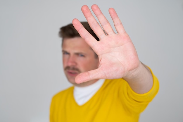 Homem maduro olhando sério mostrando palma aberta fazendo gesto de parada