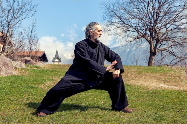 Homem maduro praticando a disciplina tai chi ao ar livre em um parque do lago em um dia de inverno